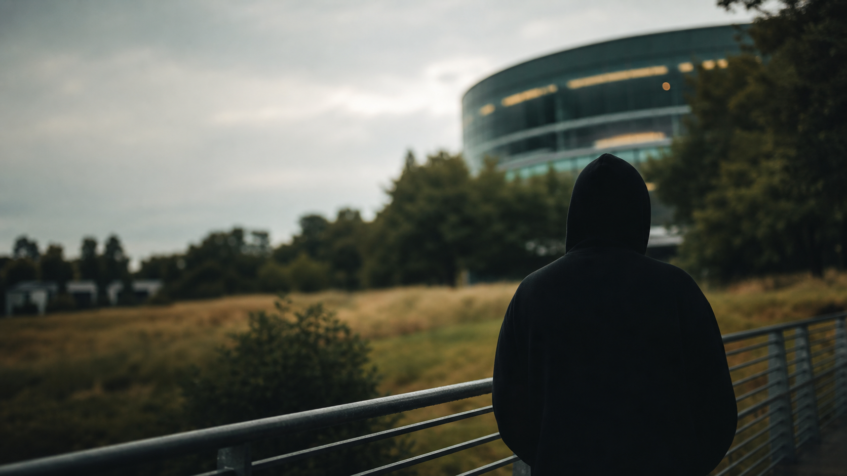 Hooded creator looking toward a blurred building and green landscape